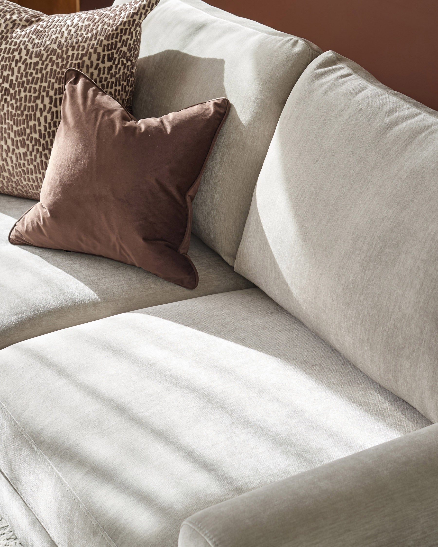 Jacob 3-seater sofa in light grey fabric with decorative pillows, angled view showing cushioned seating and armrest detail.