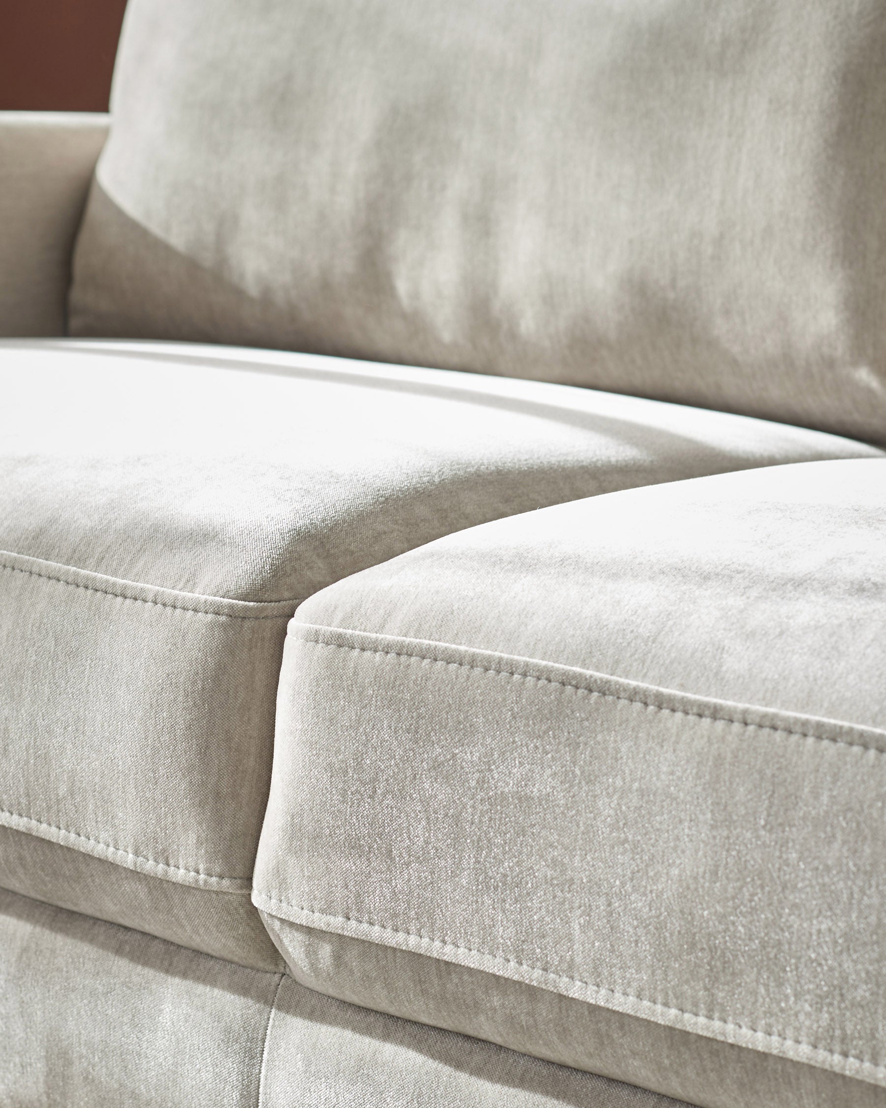 Light grey fabric 3-seater sofa with white piping detail and plush cushions, close-up side view.