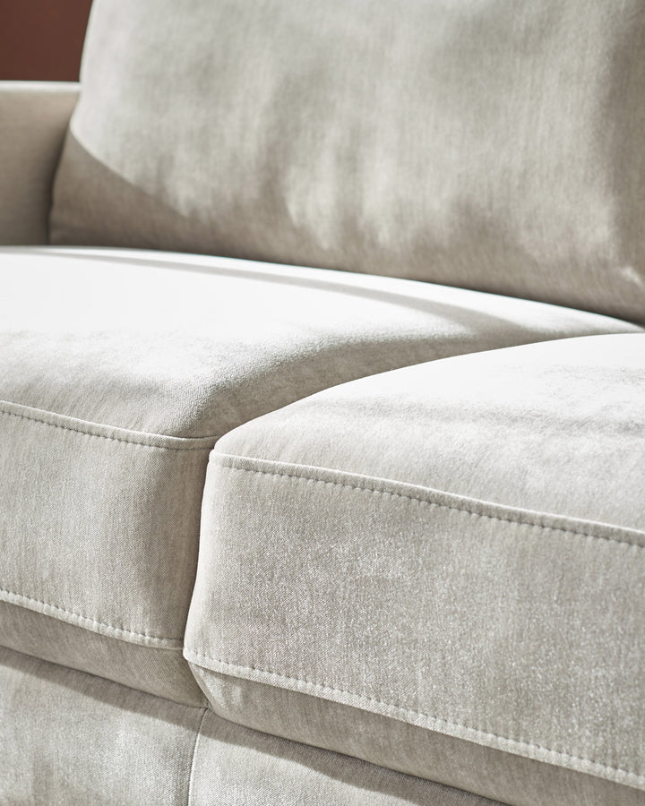 Light grey fabric 3-seater sofa with white piping detail and plush cushions, close-up side view.