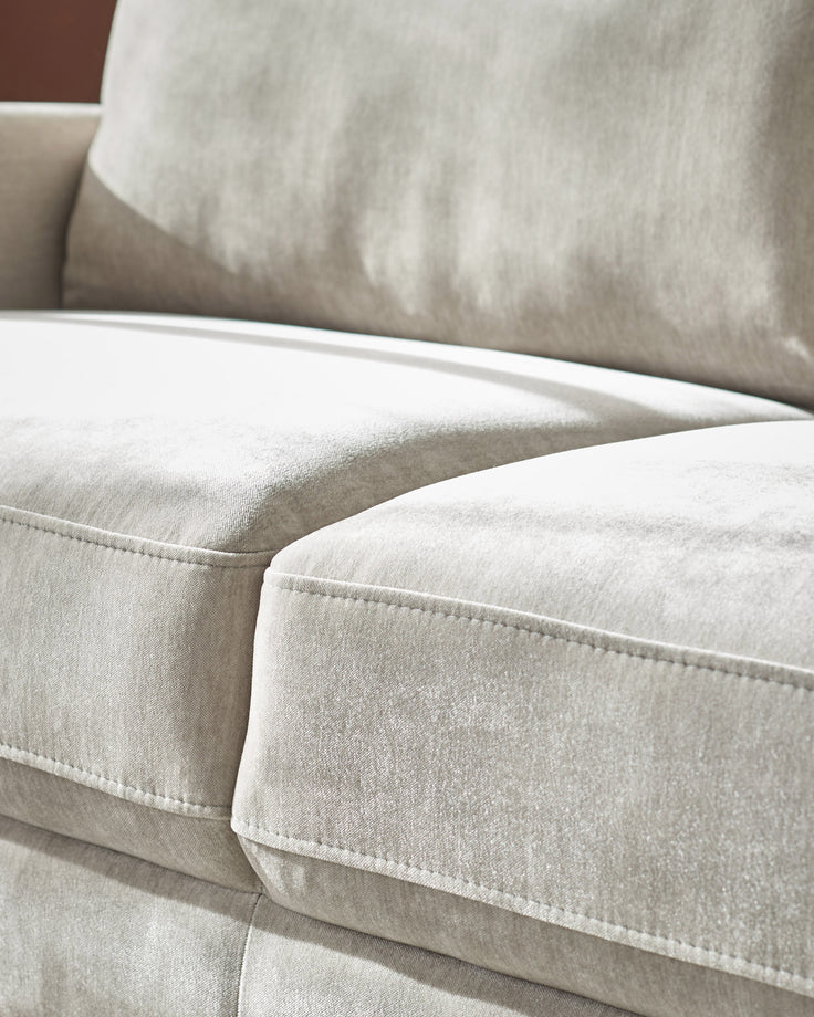 Light grey fabric 3-seater sofa with white piping detail and plush cushions, close-up side view.