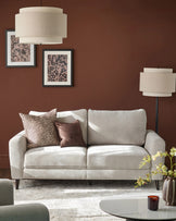 Light grey three-seater sofa with curved arms and dark wooden legs, styled in a warm terracotta room with decorative pillows.