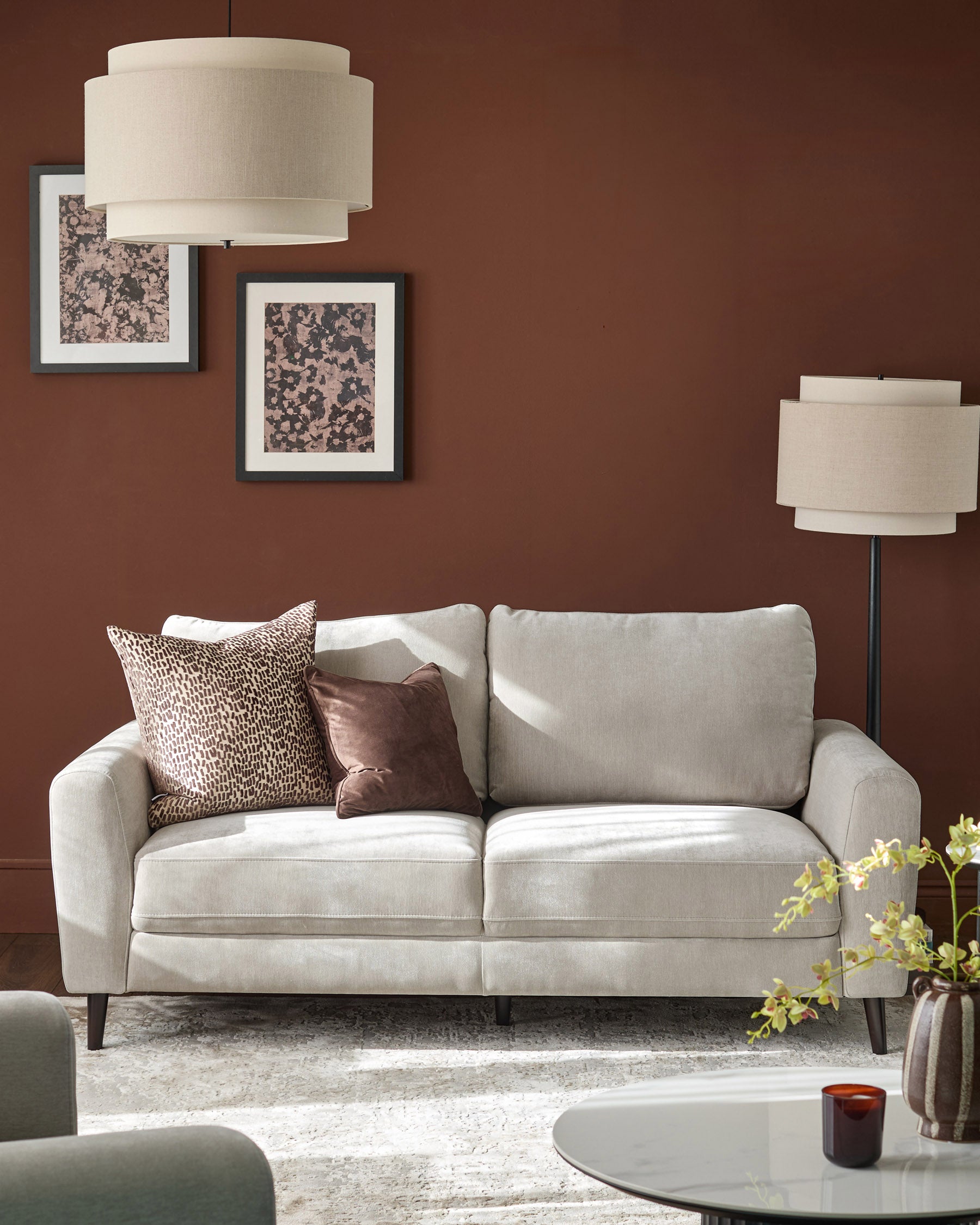 Light grey three-seater sofa with curved arms and dark wooden legs, styled in a warm terracotta room with decorative pillows.