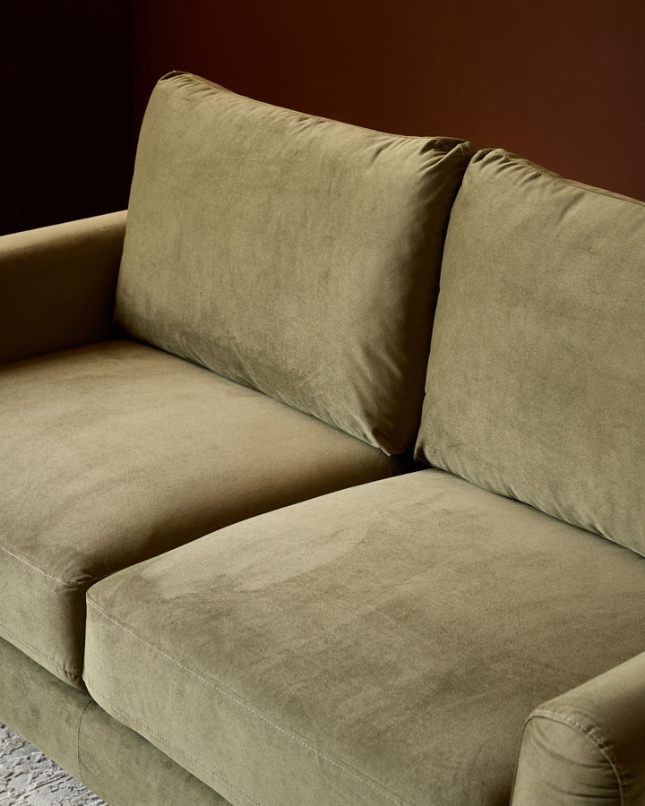 Jacob 3-seater sofa in olive green velvet, angled side view showing cushioned seat and backrest against warm background.