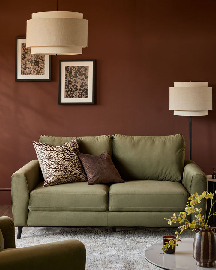 Jacob three-seater sofa in olive green velvet, displayed in a styled living room setting with accent pillows.