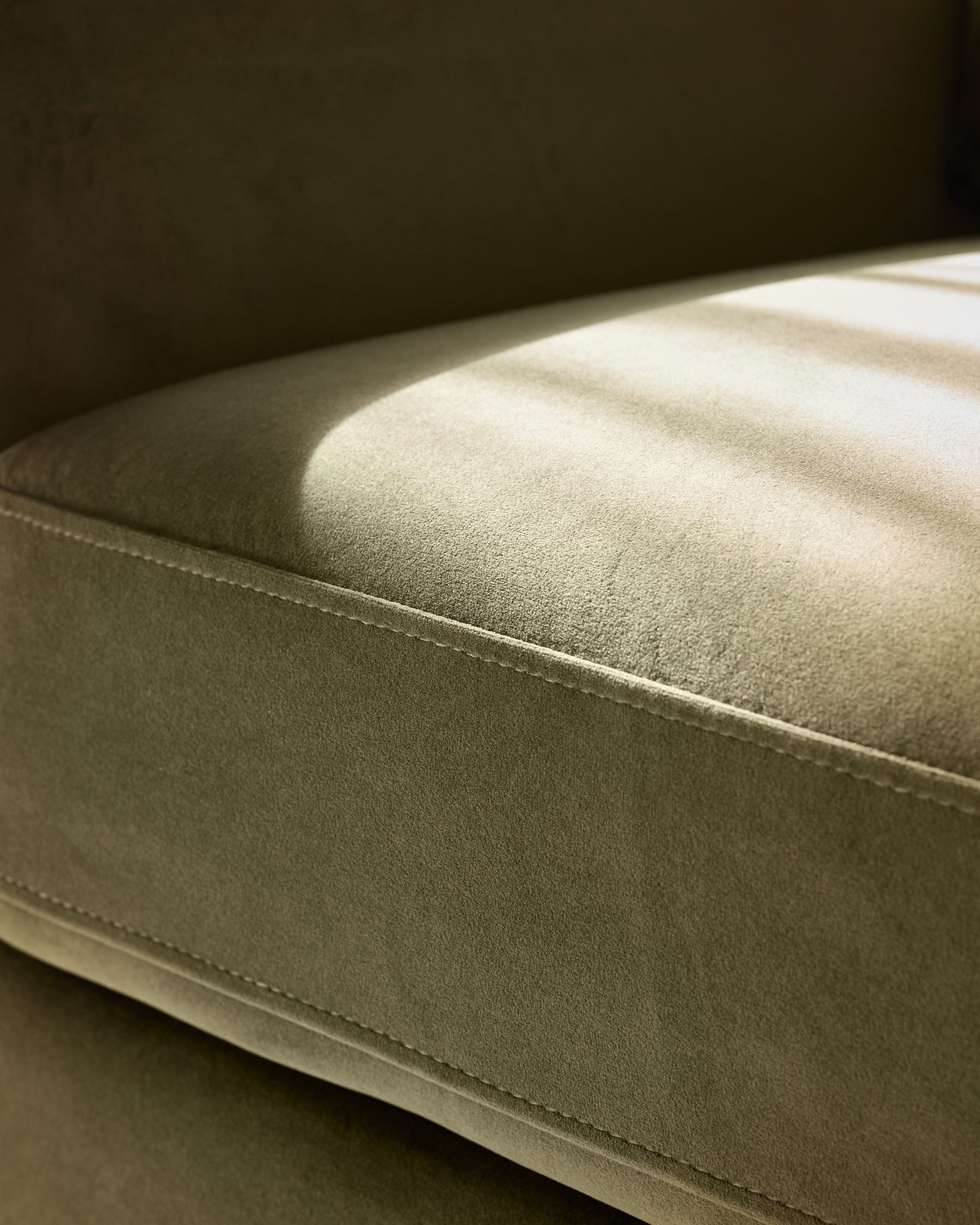 Jacob armchair in olive-green velvet, close-up side view showing plush upholstery and stitched seam detail.