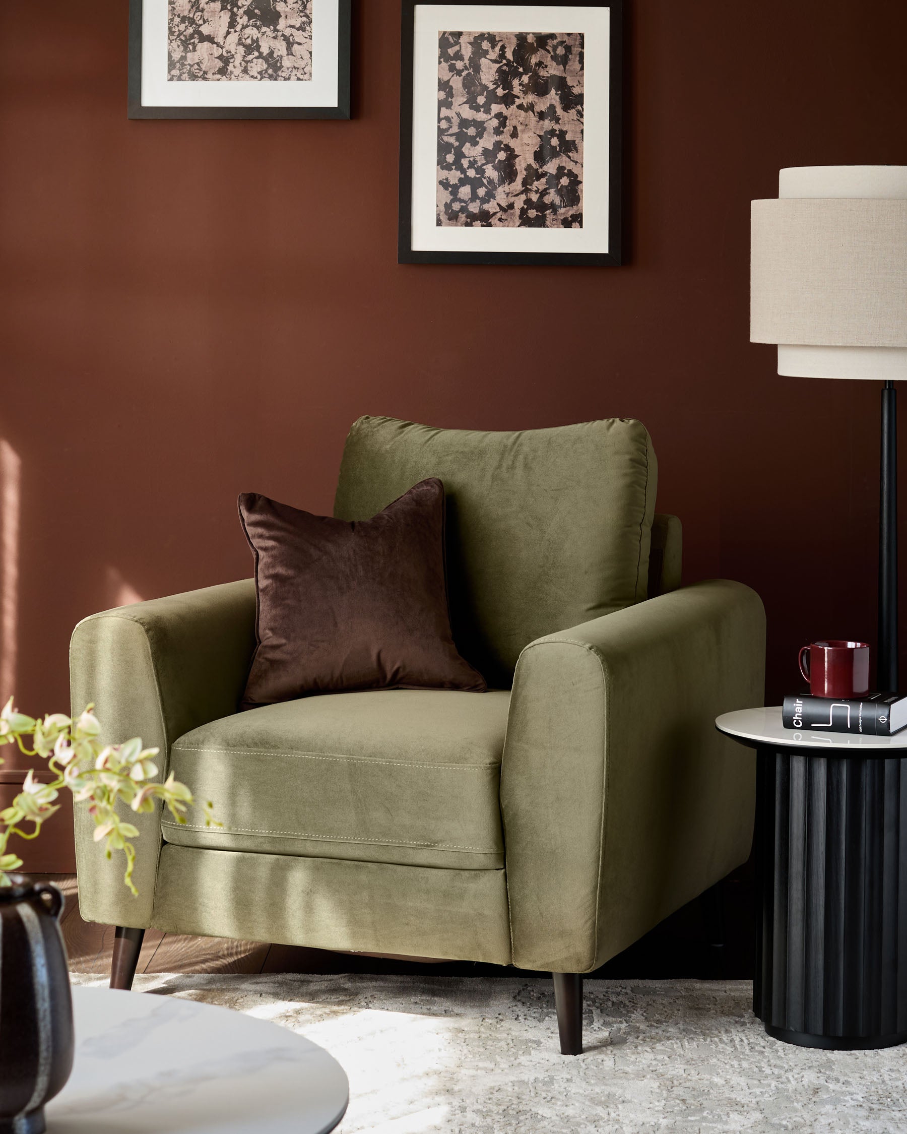 Jacob armchair in olive green velvet with dark wood legs, styled with a brown cushion against a burgundy wall.