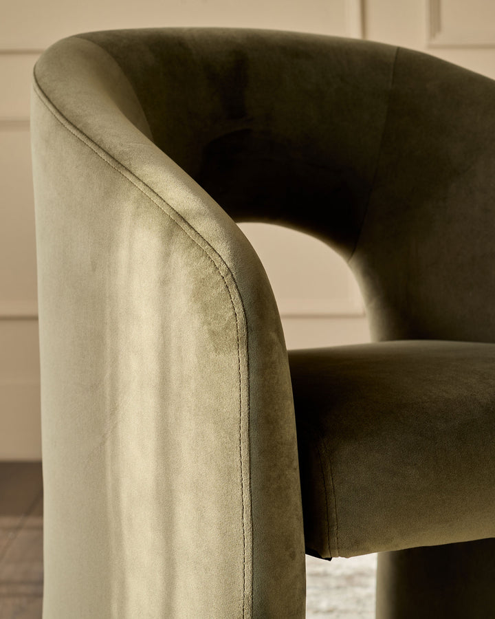 Jasper dining chair in olive green velvet, showing curved armrest and seat detail from side angle.