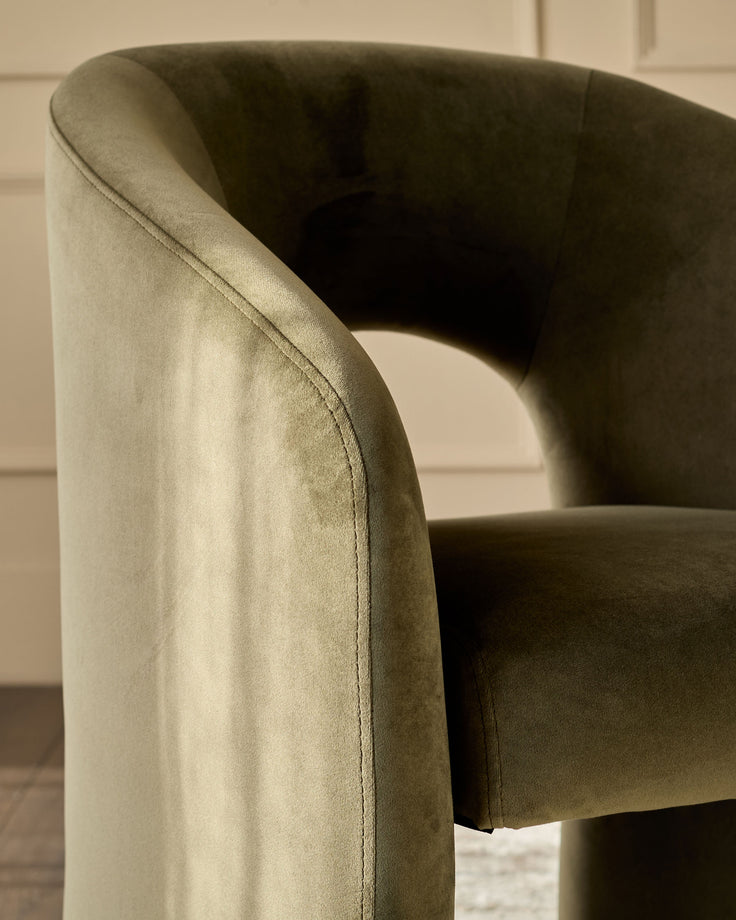 Jasper dining chair in olive green velvet, showing curved armrest and seat detail from side angle.
