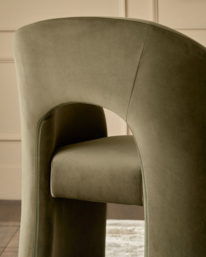Jasper dining chair in olive green velvet, side angle view showing curved backrest and cylindrical armrest detail.