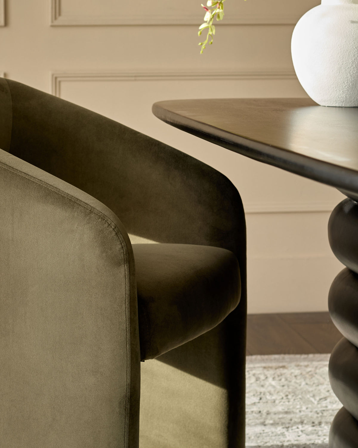 Jasper dining chair in olive green velvet, shown from side angle with curved backrest and rounded armrests.