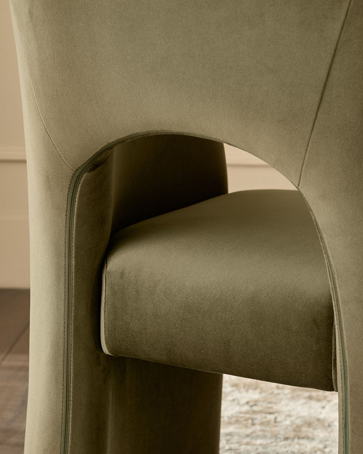 Jasper dining chair in olive green velvet, close-up of curved backrest and armrest detail.