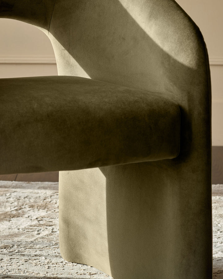 Jasper dining chair in olive green velvet, side view showing curved backrest and armrest detail.
