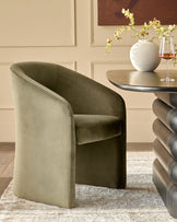 Jasper dining chair in olive green velvet, shown at an angle beside a round table with floral arrangement and wine glass.