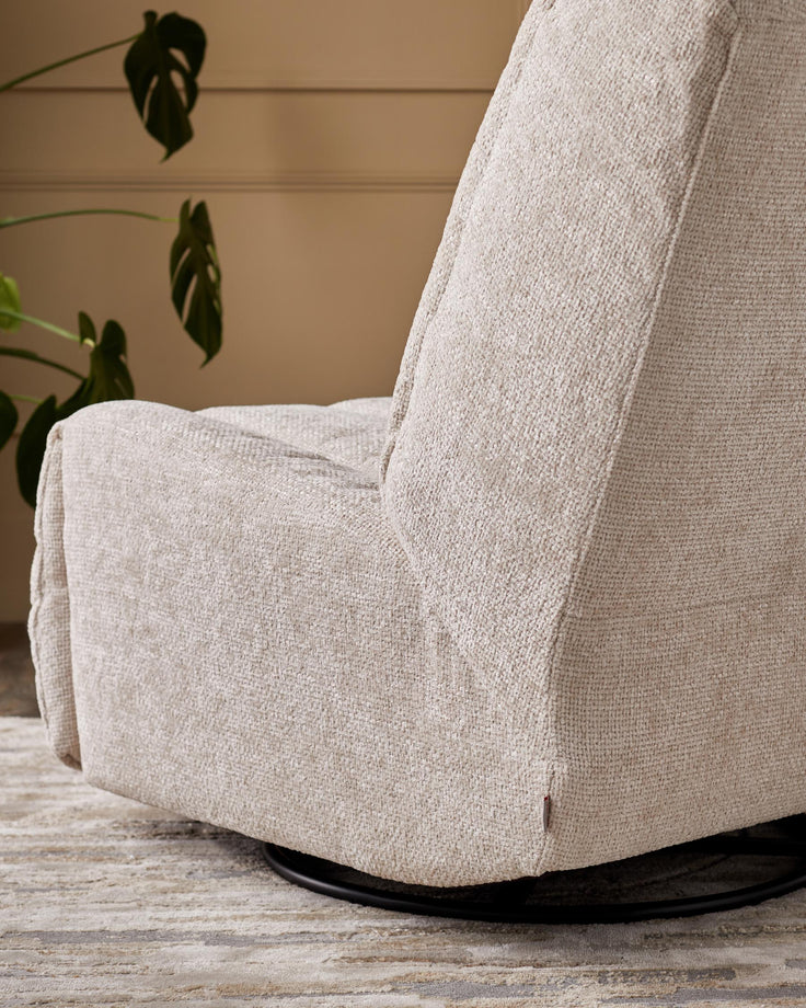 Close-up of a modern, swivel armchair with textured, light-beige fabric. A Monstera plant is in the background.