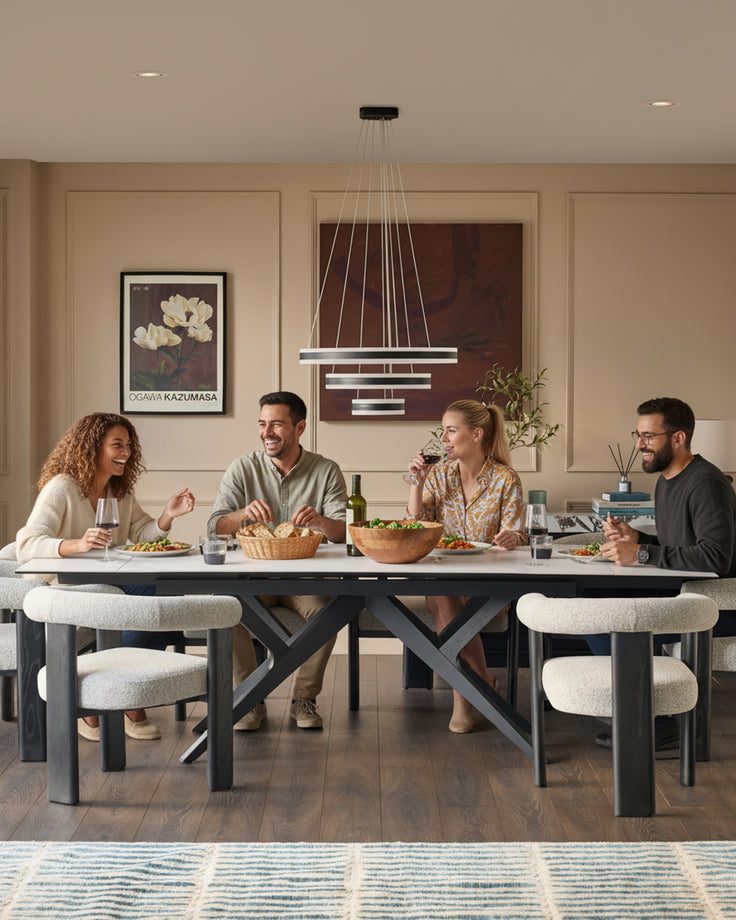 Jennet extending dining table in white ceramic with black X-frame base, seated by four people during a dinner gathering.