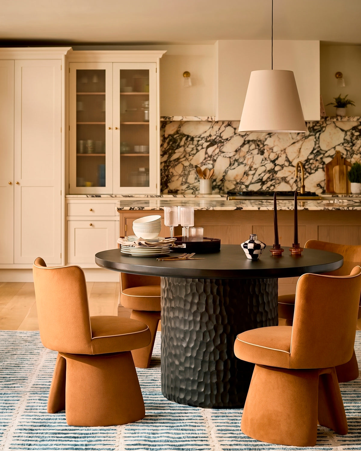 Jenna swivel dining chair in caramel fabric, shown in a modern kitchen setting around a black round table.