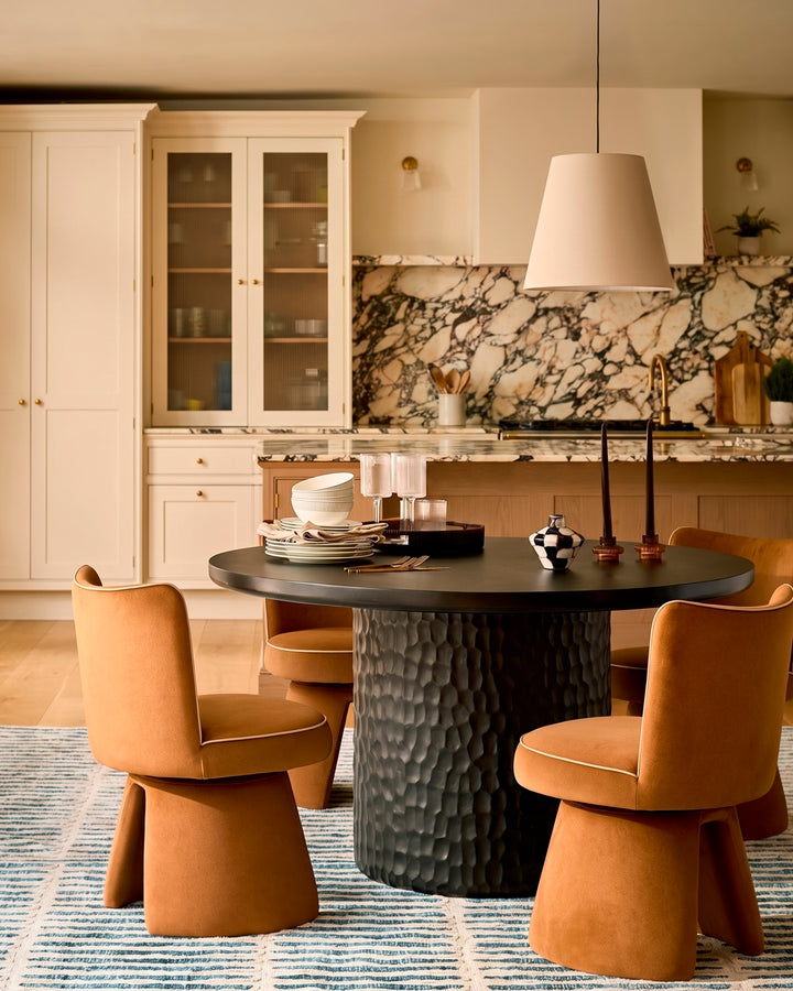 Jenna swivel dining chair in caramel fabric, shown in a modern kitchen setting around a black round table.