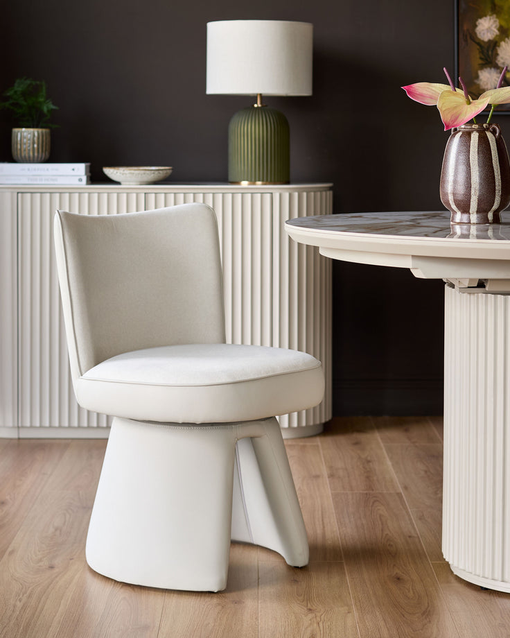 Jenna swivel dining chair in cream fabric with light grey accents, shown in a styled room setting with round table and dresser.