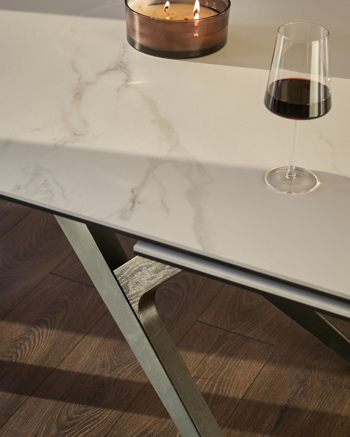 White marble-effect extending dining table with brushed metal leg detail, styled with wine glass and candle.