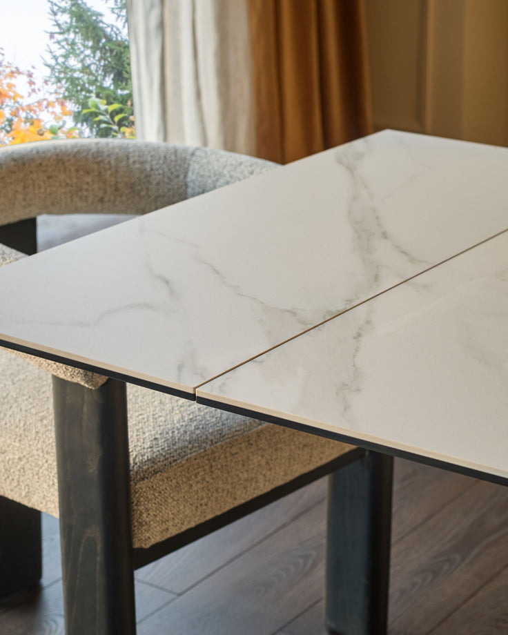 Jennet extending dining table with white marble-effect ceramic top and black metal frame, shown extended in a modern room setting.