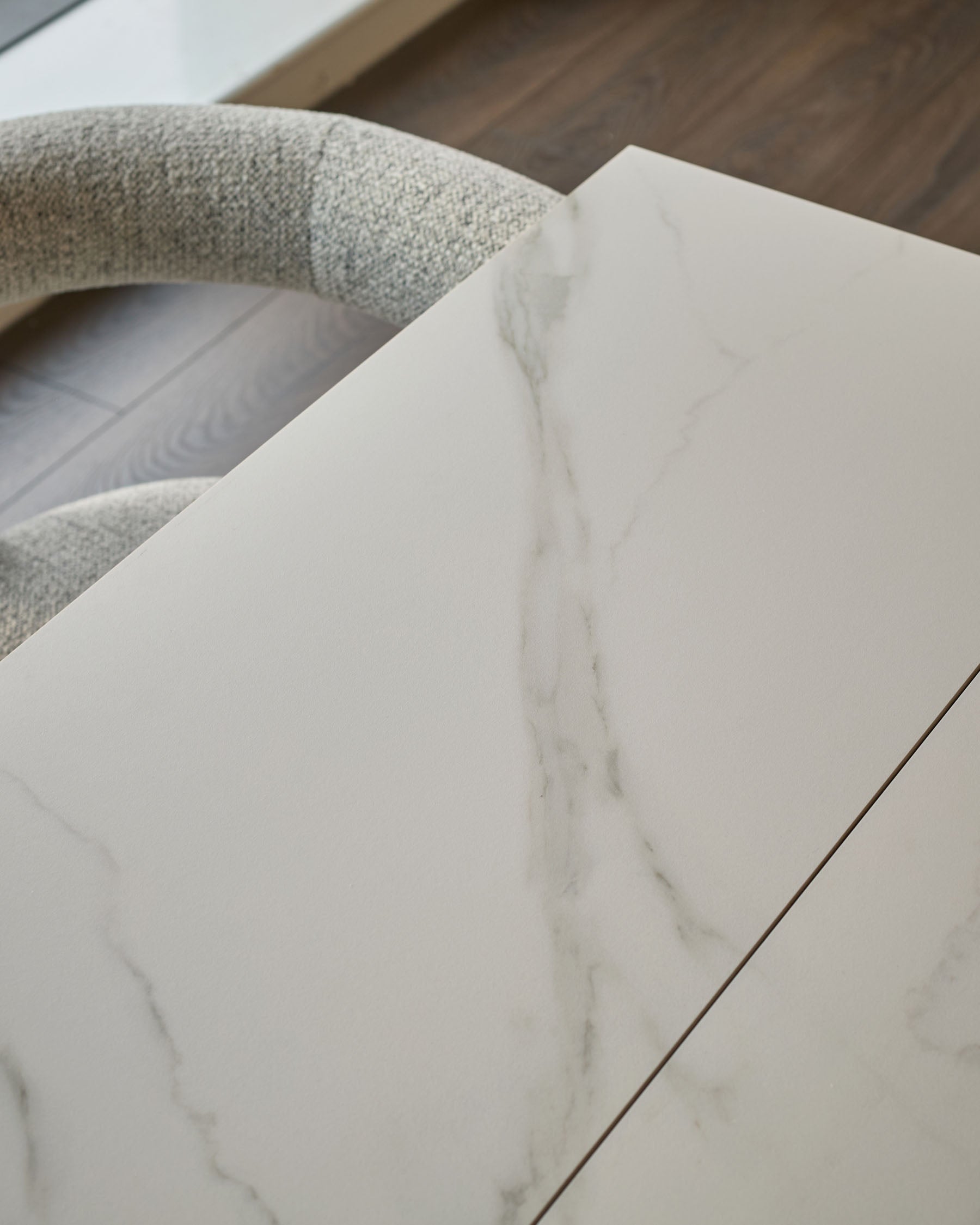 White marble-effect ceramic dining table top with textured Grey fabric chair back visible above.