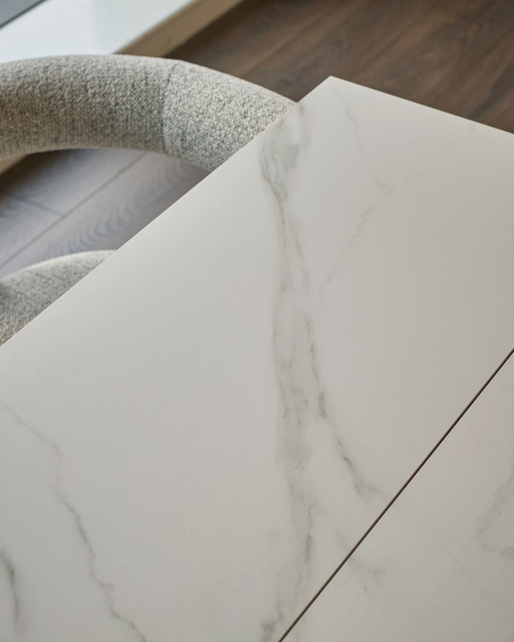 White marble-effect ceramic dining table top with textured Grey fabric chair back visible above.