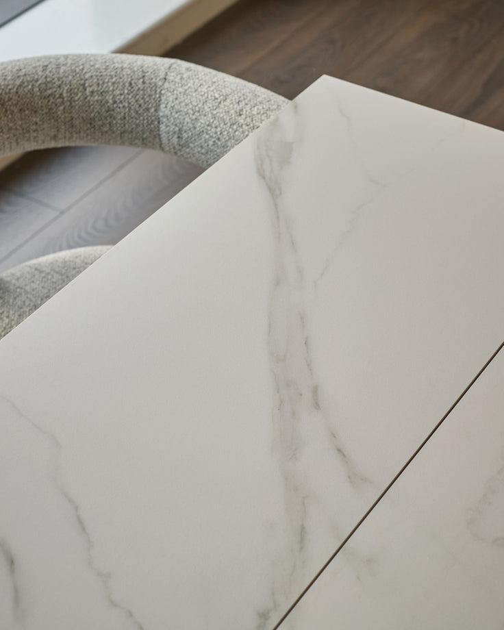 White marble-effect ceramic dining table top with textured Grey fabric chair back visible above.