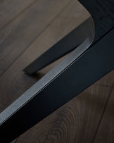 Black handle detail on extending dining table with brushed metal finish and dark wood surface.