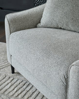 Grey fabric armchair with black wooden legs on striped grey rug, angled side view showing curved arm and seat detail.