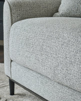 Grey fabric armchair with textured upholstery and dark wooden legs, shown in close-up detail.