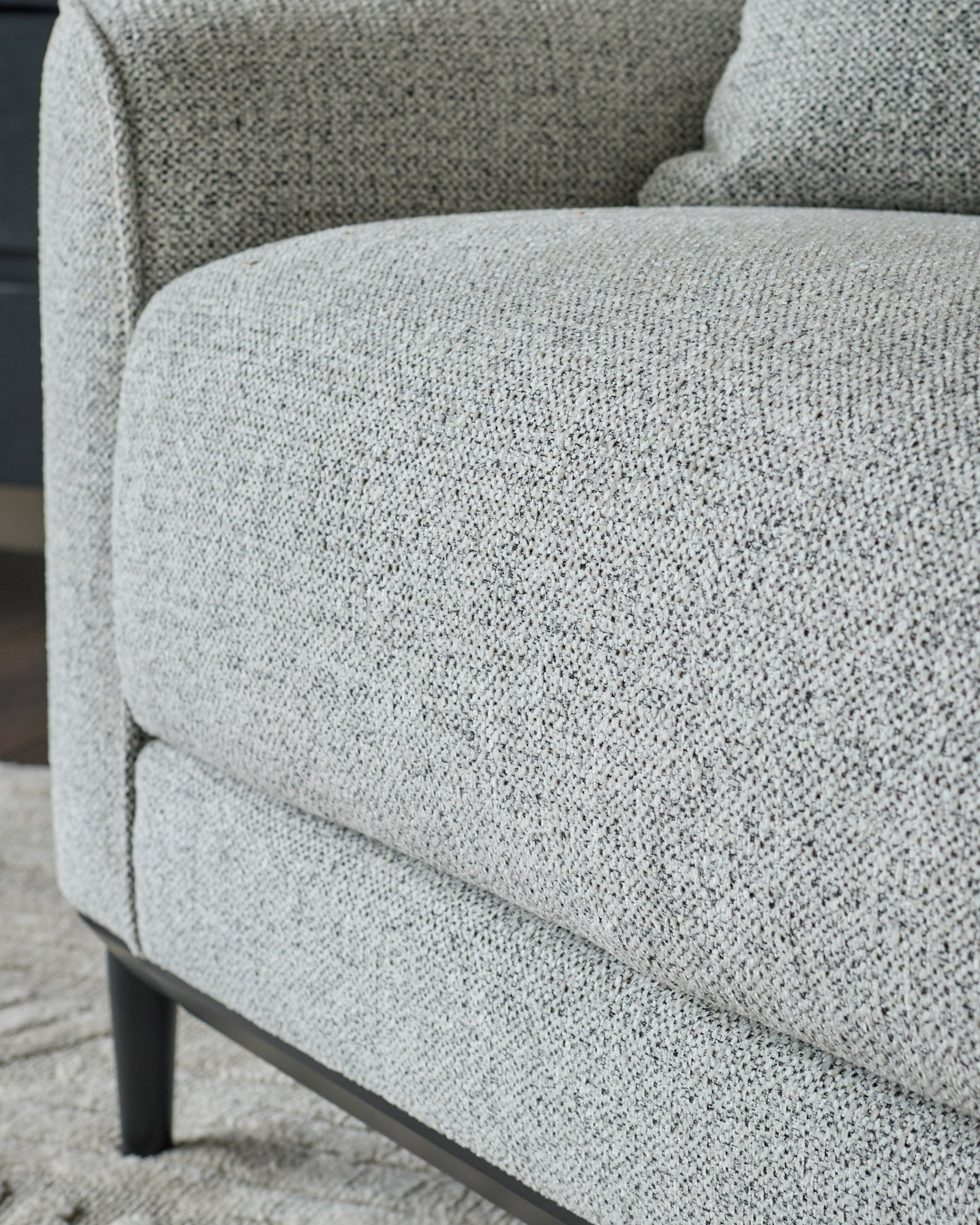 Grey fabric armchair with textured upholstery and dark wooden legs, shown in close-up detail.