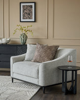 Grey upholstered armchair with black wooden legs, shown in a styled living room setting with decorative pillows.