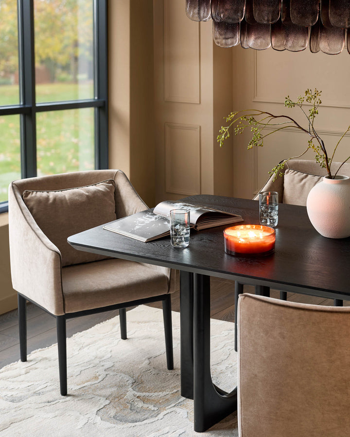 Champagne fabric dining chair with curved backrest and black wooden legs, shown at black table in modern interior.