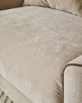 Champagne fabric armchair with soft upholstery and piped edge detail visible on the armrest.
