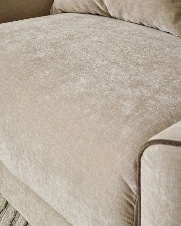Champagne fabric armchair with soft upholstery and piped edge detail visible on the armrest.