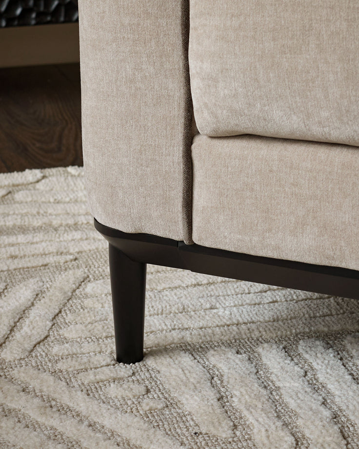 Champagne fabric armchair with black wooden leg, shown at an angle on a cream patterned rug.