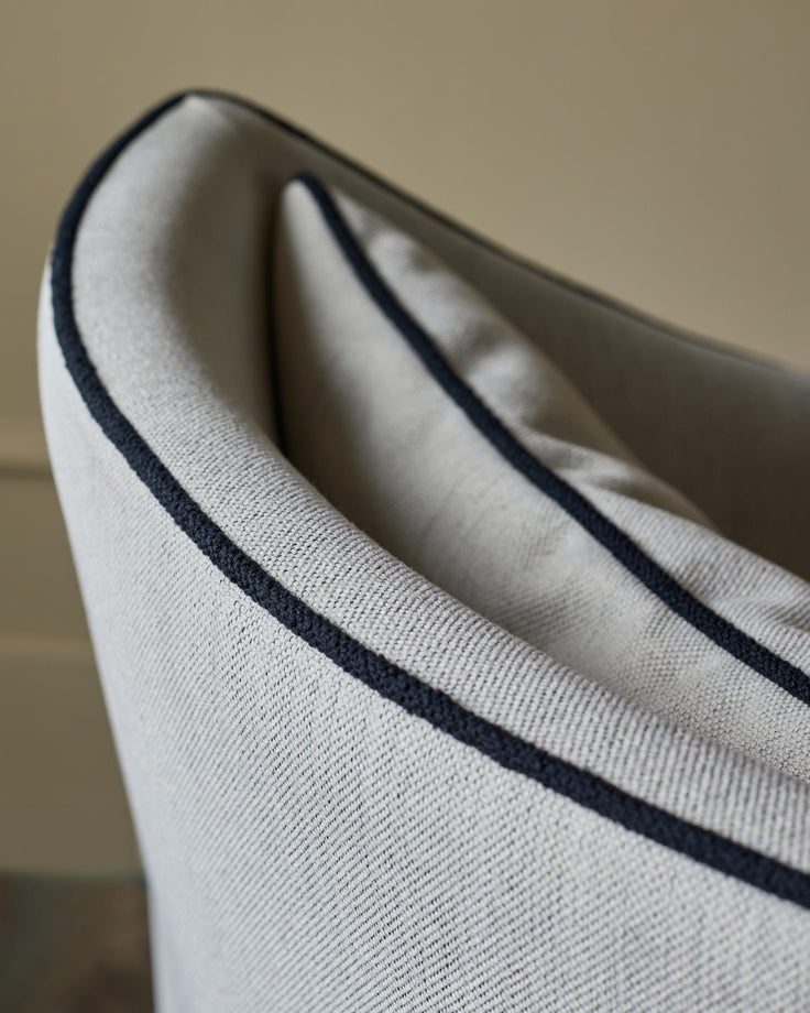 Close-up of a stylish armchair with a neutral fabric and a contrasting dark trim, perfect for a modern living space.