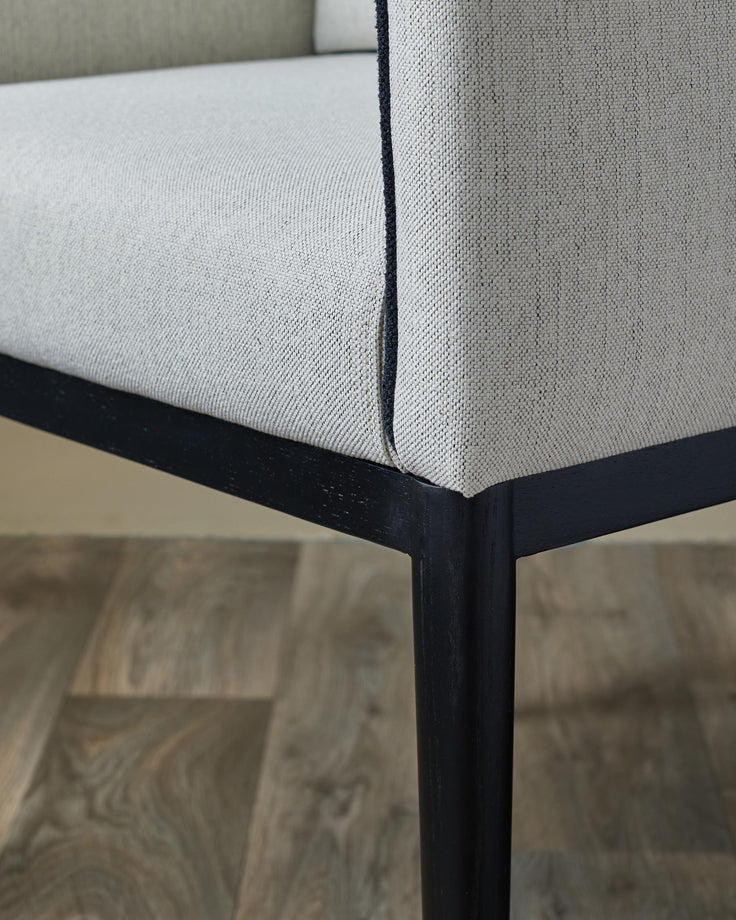Close up of a chair with light upholstery and a black frame, showing the seat and leg.