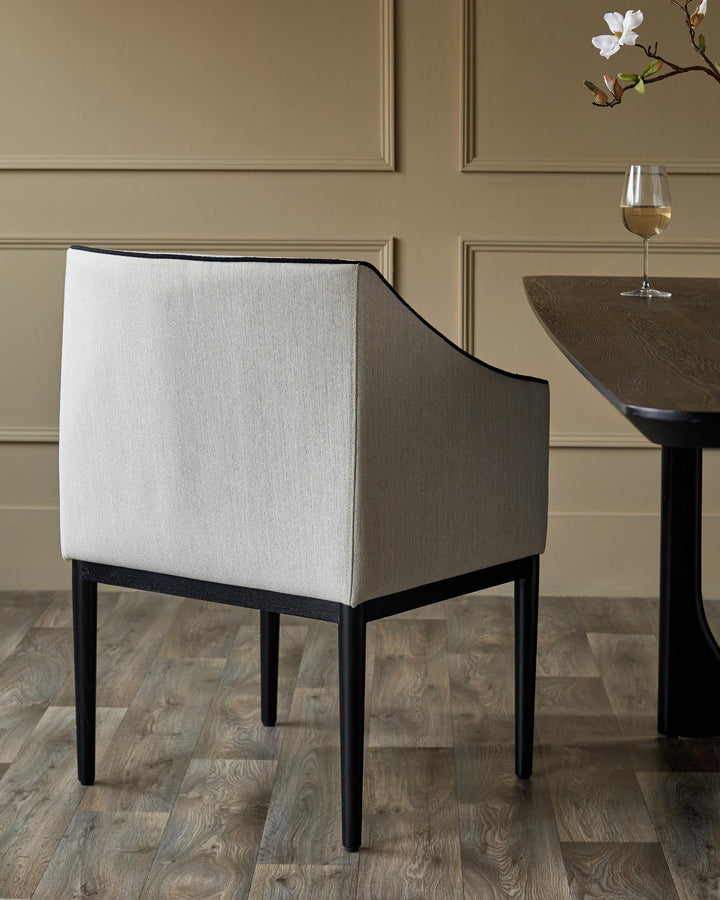 Upholstered dining chair with black frame and table with wine glass and floral decoration.