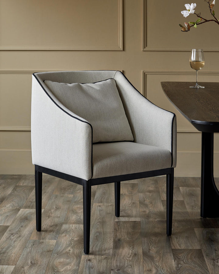A stylish grey armchair with black trim and legs, positioned next to a wooden table with a glass of wine.