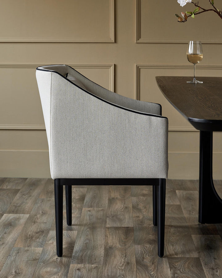 An upholstered dining chair with a dark wood table and wine glass beside it.
