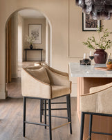 Honey fabric bar stool with black metal legs and brass footrest in modern kitchen setting.