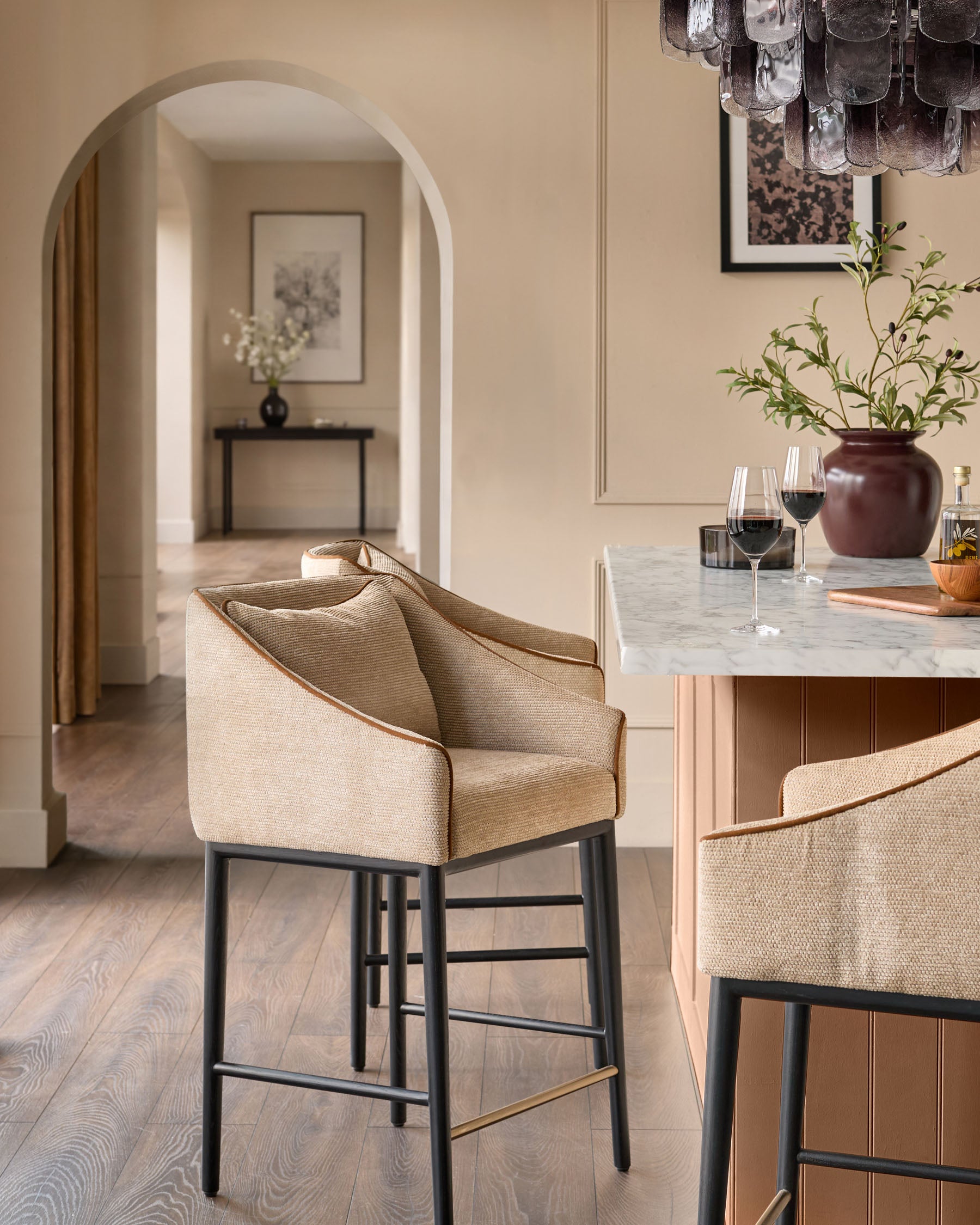 Honey fabric bar stool with black metal legs and brass footrest in modern kitchen setting.