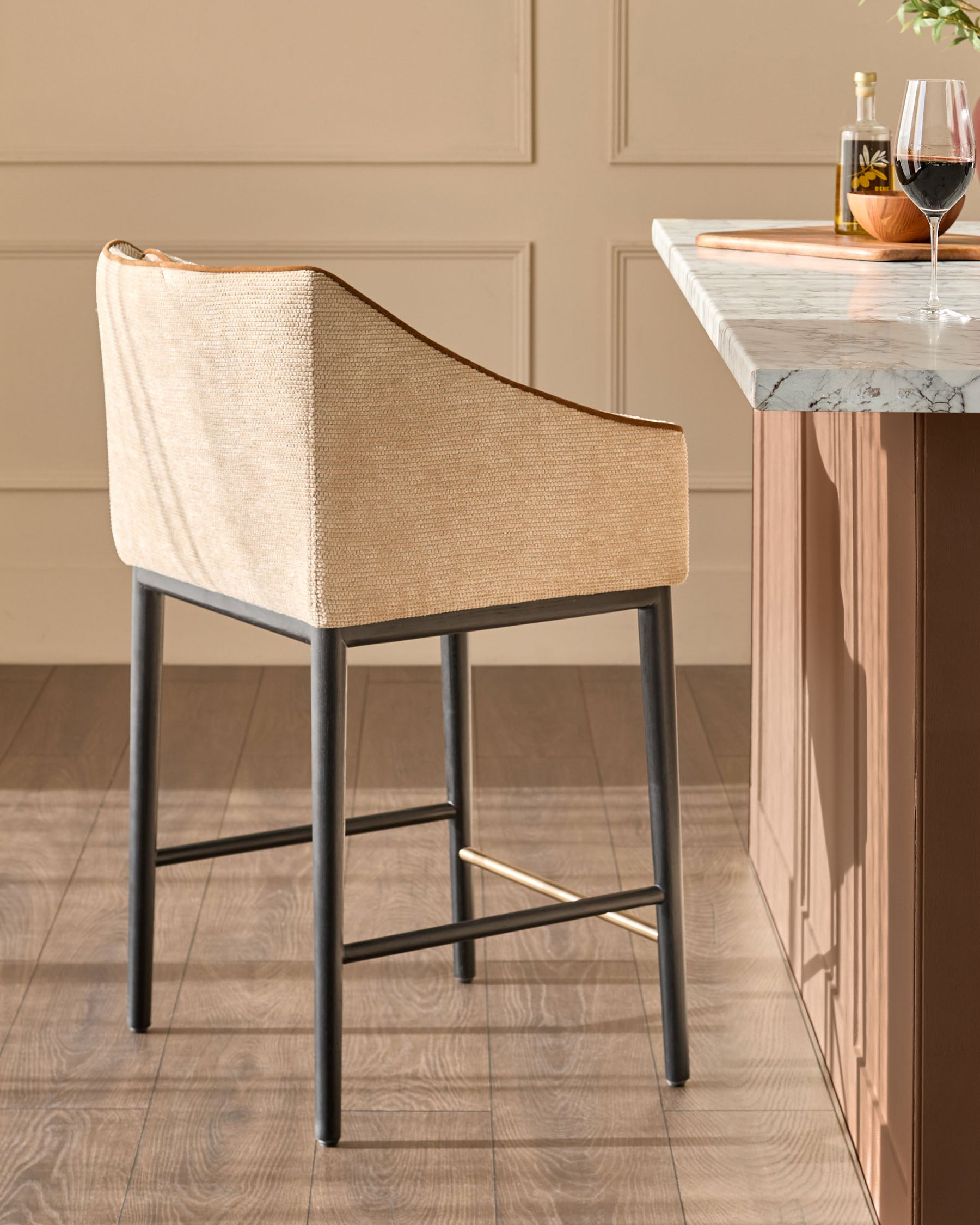 Julep bar stool in honey fabric with black metal legs and footrest, shown from side angle next to marble-top counter.