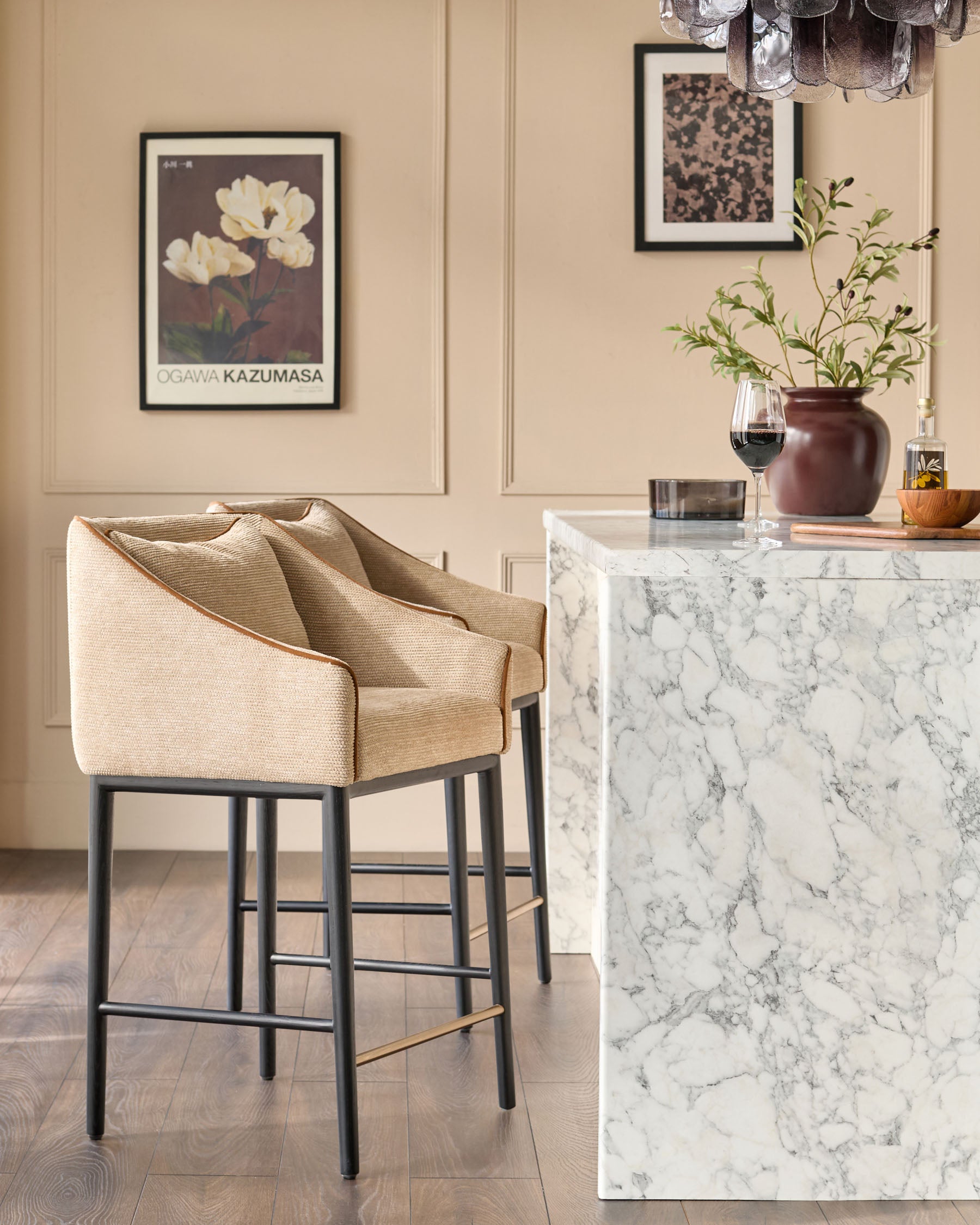 Honey fabric bar stool with black metal legs and brass footrest, shown at marble kitchen island in elegant interior setting.