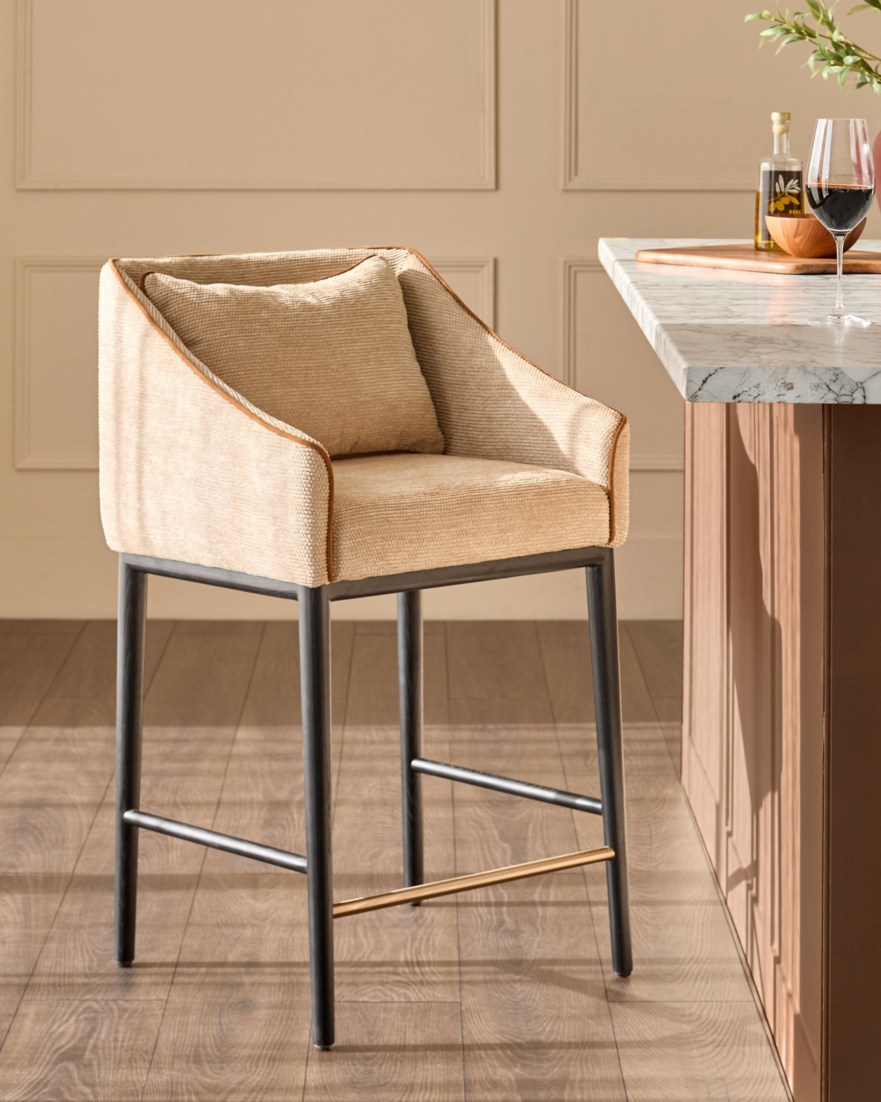 Julep bar stool in honey fabric with black metal legs and brass footrest, positioned at a marble-top counter.
