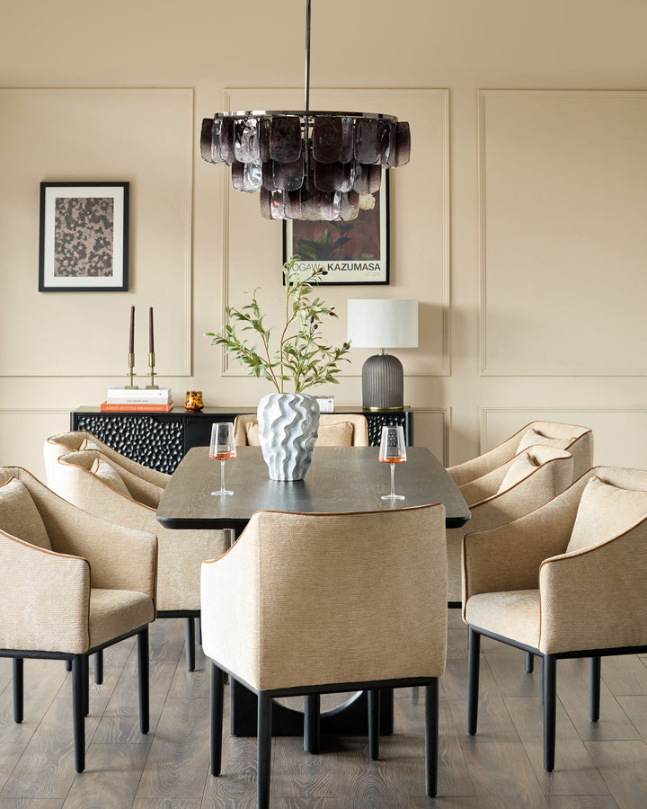 Honey-colored fabric dining chair with black legs, shown in an elegant dining room setting around a round table.