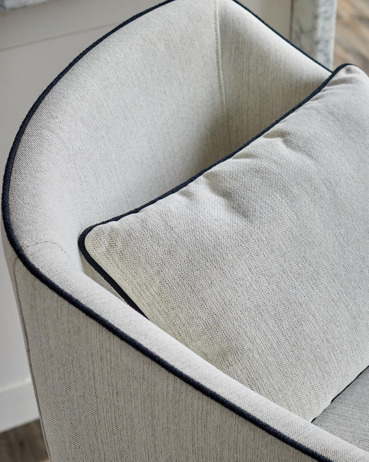 An upholstered chair, with a square cushion in a similar material. Both feature dark blue piping.