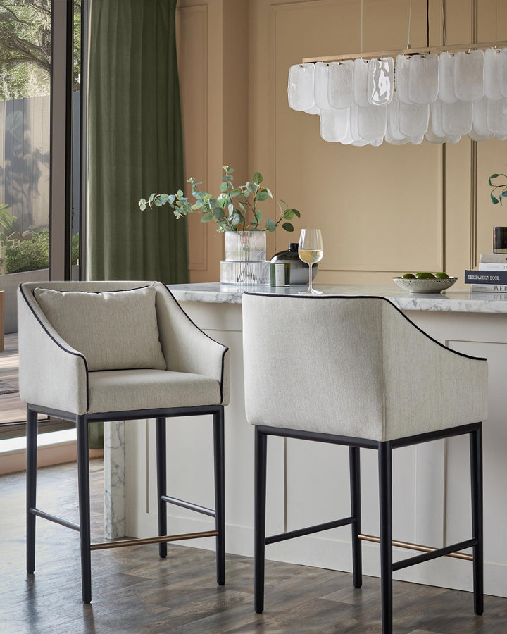 Two modern bar stools with upholstered seats and sleek black frames sit at a kitchen island, exuding contemporary elegance.