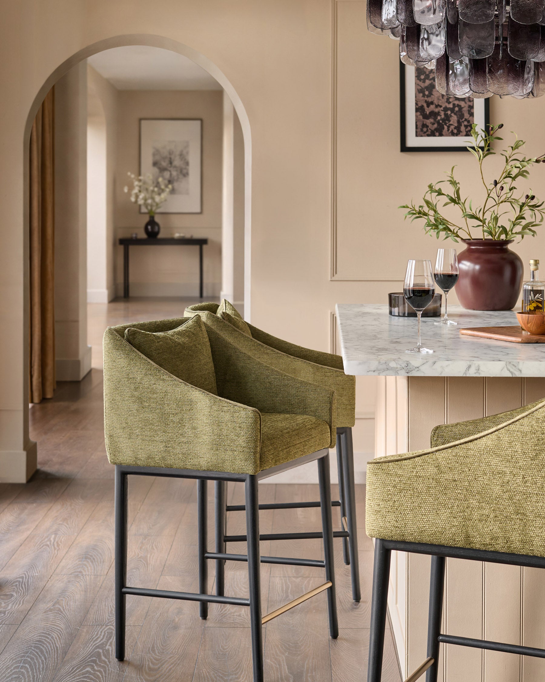 Olive green upholstered bar stool with black metal frame and footrest, shown at kitchen island in elegant dining space.